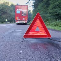 Red warning triangle on a road with a broken down truck.