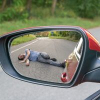 Hit and run concept. View on injured man on road in rear mirror